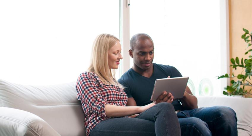Couple sitting on sofa, both looking at an ipad.