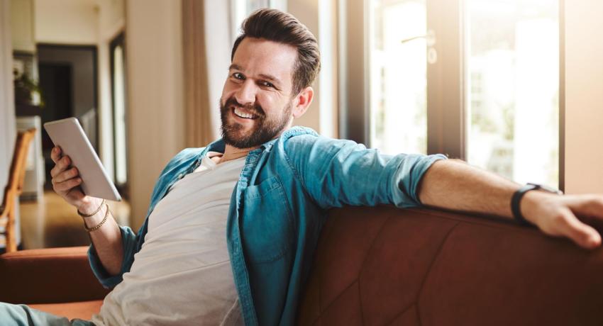 Man smiling, sitting on sofa, holding ipad