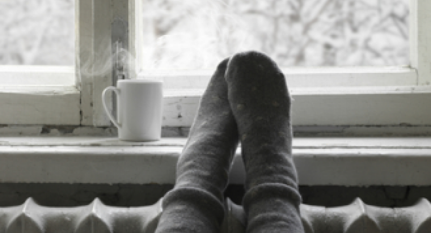 Photo of feet in socks elevated on radiator, next to mug with hot beverage