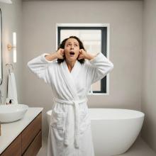 Photo of woman standing in bathroom, covering her ears with her hands