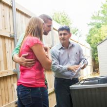 members in back yard looking at air conditioner with technician