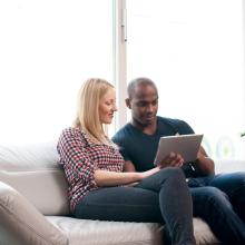 Couple sitting on sofa, both looking at an ipad.