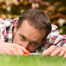 Photo of man, lying on lawn, cutting grass with scissors