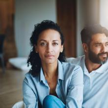 Photo of woman looking at camera, man sitting behind her looking away