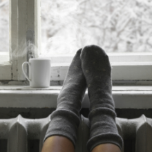 Photo of feet in socks elevated on radiator, next to mug with hot beverage
